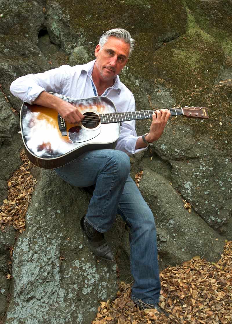 A man sitting on a rock with an acoustic guitar.